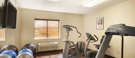 A fitness room with exercise equipment including a treadmill, elliptical, and exercise balls.