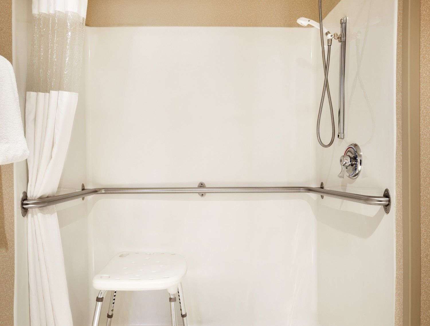 Área de duche com barra de apoio, chuveiro manual e um banquinho.