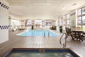 Een binnenzwembad met betegelde vloer, lounge fauteuils en een hoek voor een bubbelbad.