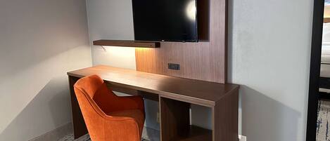 A modern office space with a desk, an orange chair, a mounted TV, and a wooden shelf.