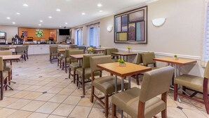 Un hall d’hôtel doté de plusieurs espaces de détente, d’un comptoir d’accueil et d’une cuisine visible au fond.