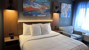 Une chambre d’hôtel avec un grand lit, deux lampes fixées au mur, un canapé et des tableaux abstraits accrochés aux murs.