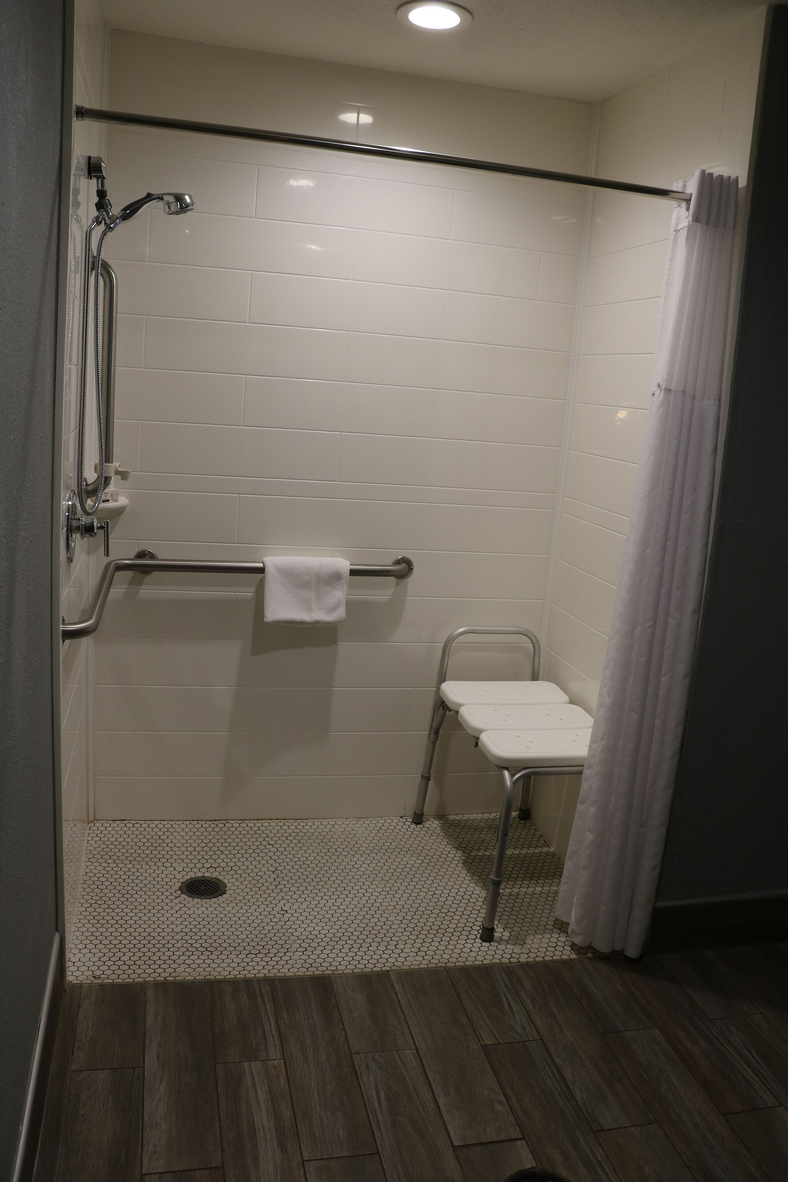 A shower area with a grab bar, a white towel, and a small white bench.