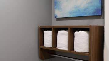 Un baño con inodoro, un perchero con tres toallas, un cuadro en la pared y una rejilla de ventilación.