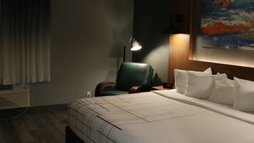 Una habitación de hotel con una cama grande, una silla verde, un escritorio con una lámpara y un cuadro en la pared.