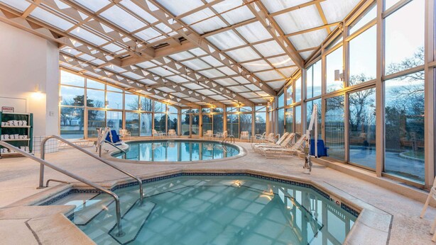 Une piscine intérieure avec des parois en verre transparent, un toit abrité et des chaises longues disposées autour de la piscine.