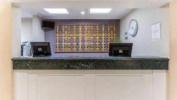 Un mostrador de recepción con encimera de mármol, un televisor de pantalla plana, un reloj y una pizarra de anuncios.