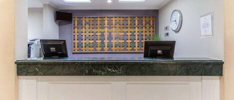 A reception desk with a marble top, a flat-screen TV, a clock, and a bulletin board.