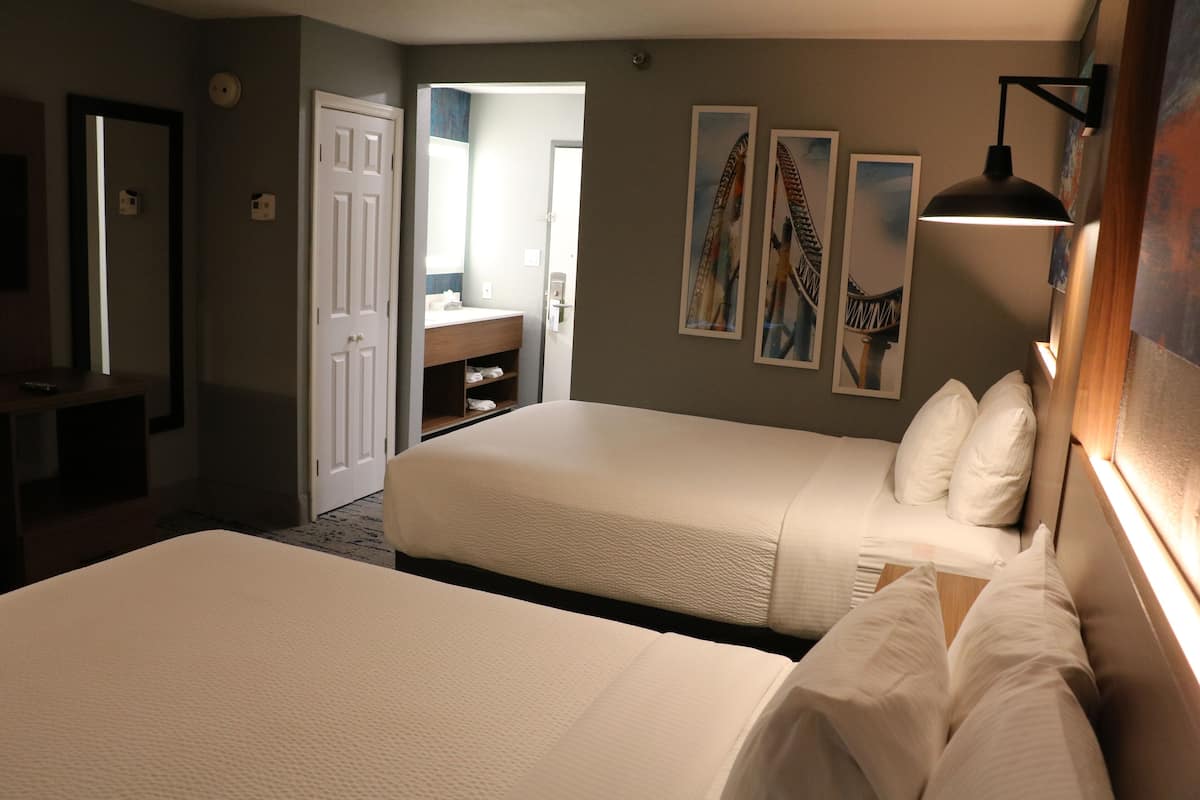 A hotel room with two beds, a bathroom, and artwork on the walls.