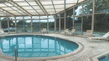 Una piscina interna con pareti di vetro trasparente, un tetto coperto e diverse poltrone attorno alla vasca.