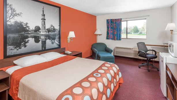 Ein Hotelzimmer mit einem Bett, Schreibtisch, Stuhl und einem großen gerahmten Bild eines Leuchtturms.