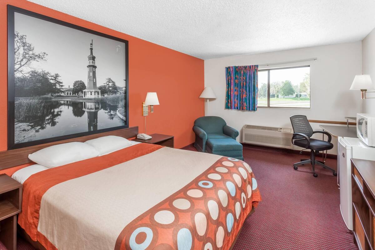 Habitación de hotel con cama, escritorio, silla y un cuadro grande con un faro.