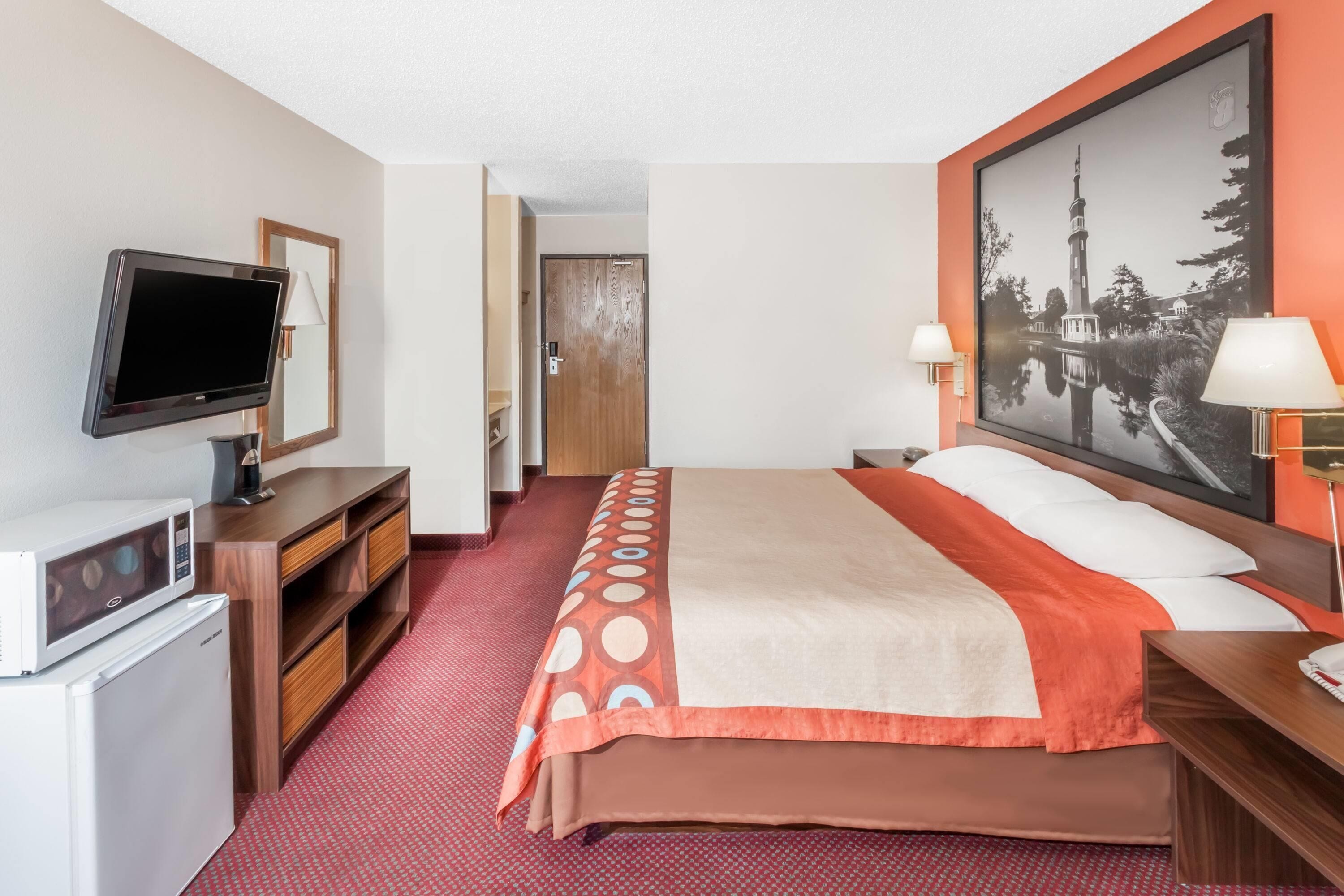 A hotel room with a bed, a television, a desk, a microwave, and a large framed picture on the wall.