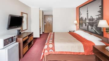 A hotel room with a bed, a television, a desk, a microwave, and a large framed picture on the wall.