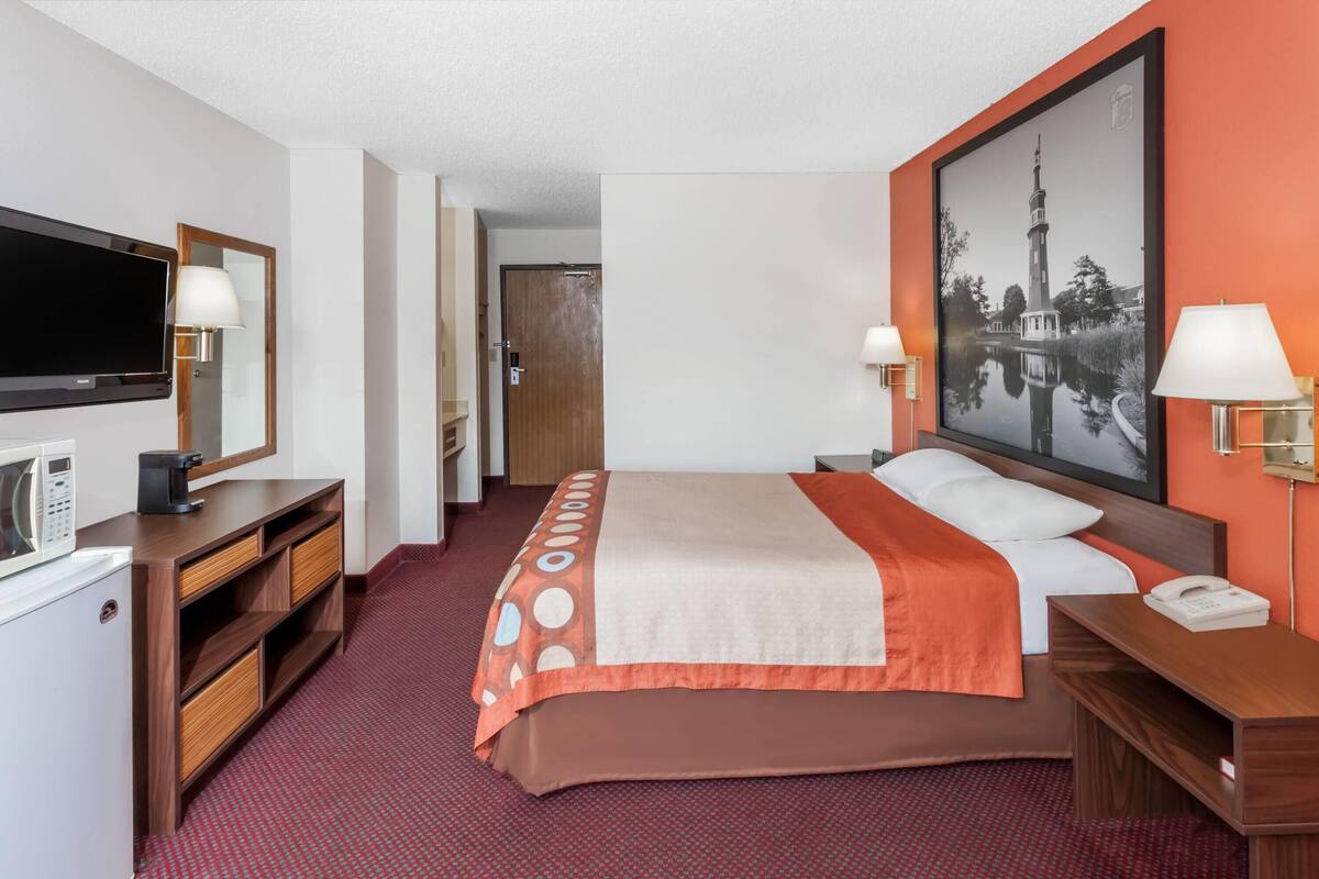 Habitación de hotel con cama, televisión, escritorio con lámpara, teléfono y microondas.