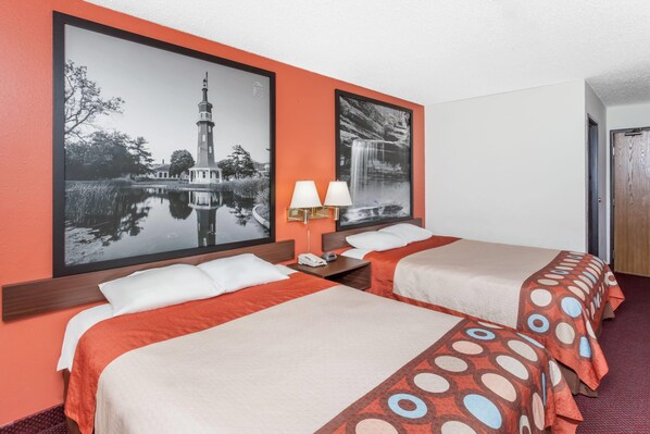 Habitación de hotel con dos camas, una mesita de noche con lámpara y dos cuadros en la pared.