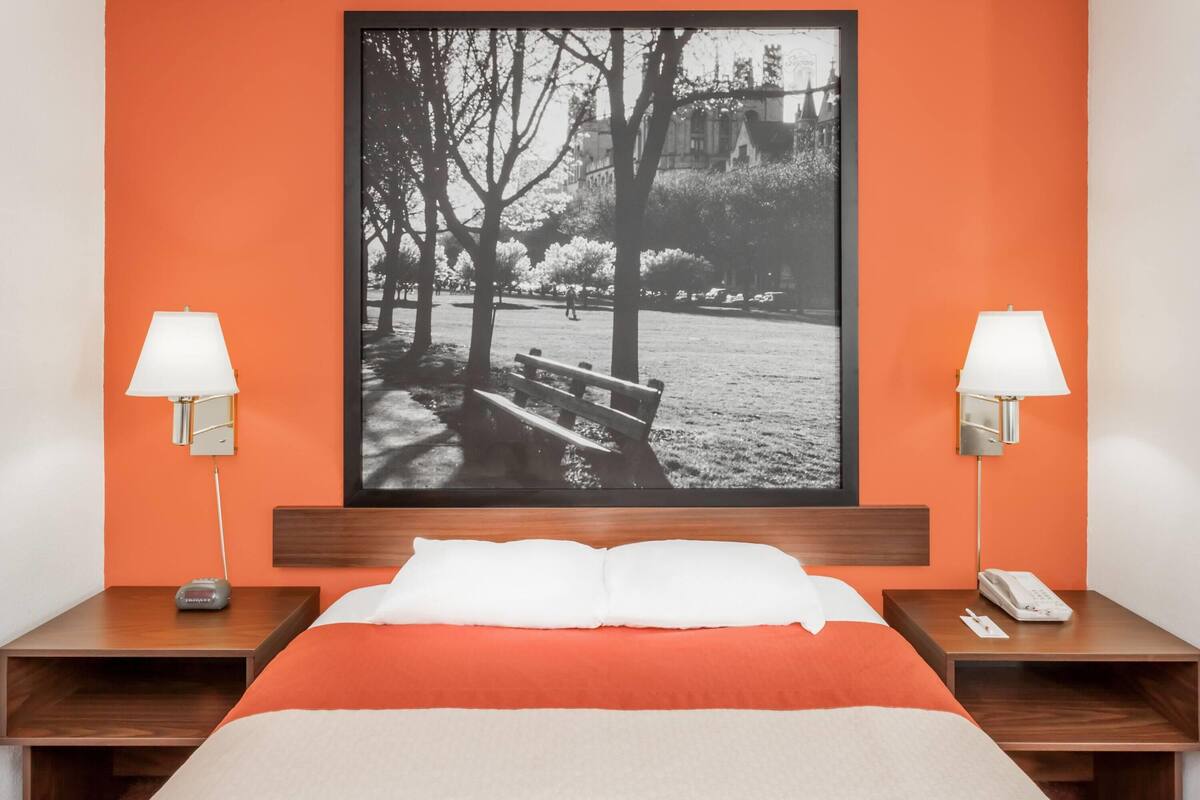 Habitación de hotel con una cama, dos mesitas de noche con lámparas, un cuadro en la pared y un cabecero de madera.