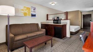 Une chambre d’hôtel compacte comprenant un canapé marron, une petite table en bois, une kitchenette avec un four à micro-ondes et un lit.