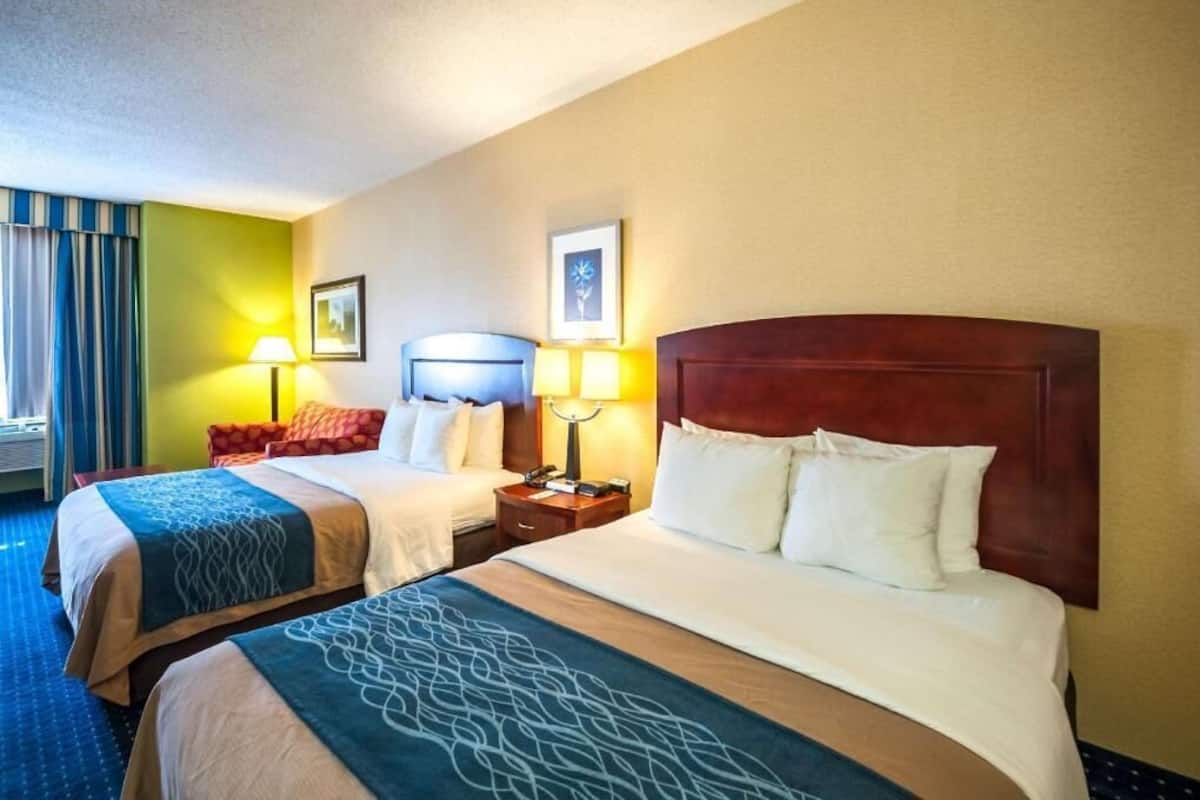A hotel room with two beds, a nightstand with lamps, and a framed picture on the wall.