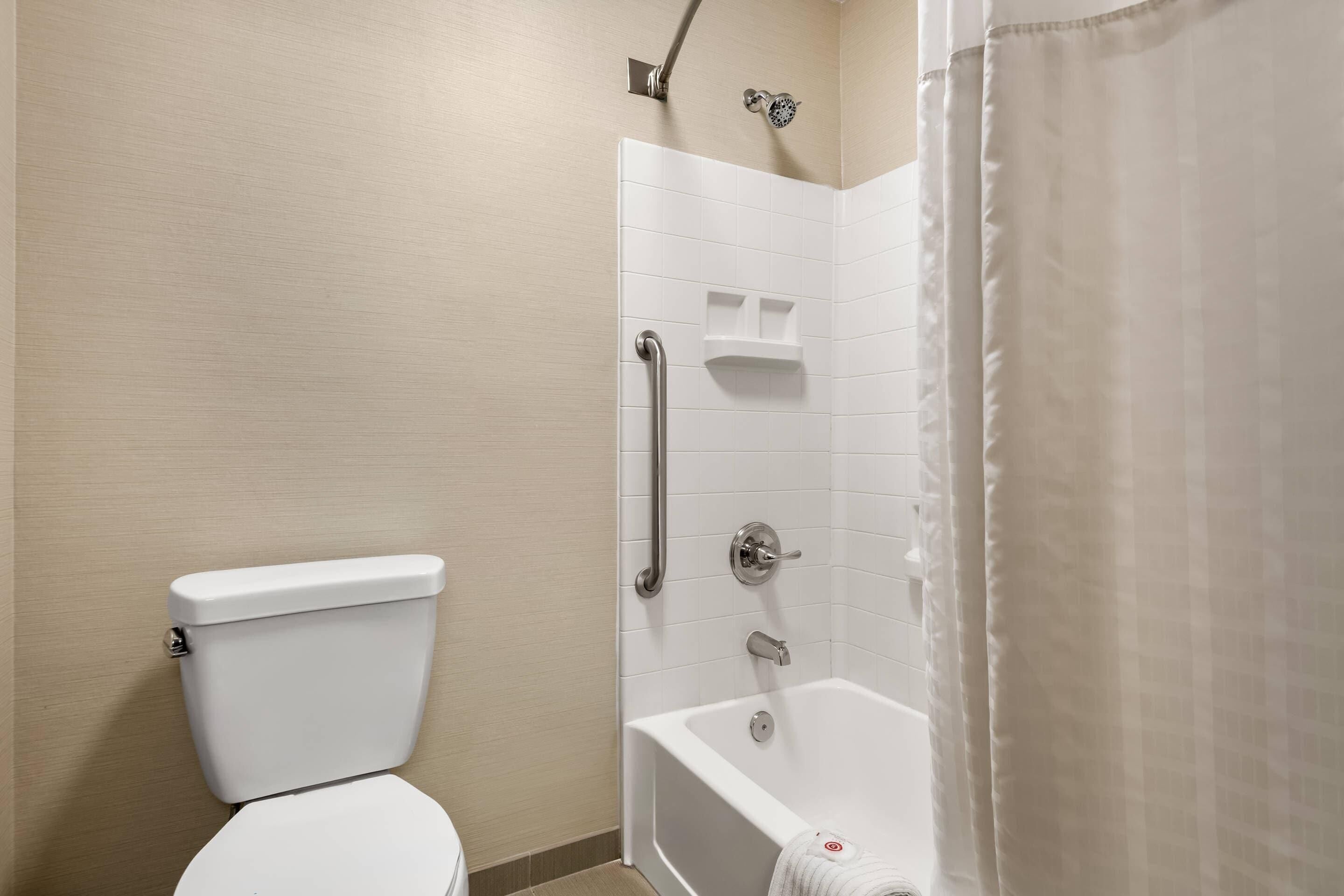 Un bagno con il water, una doccia dotata di maniglione e una vasca da bagno.