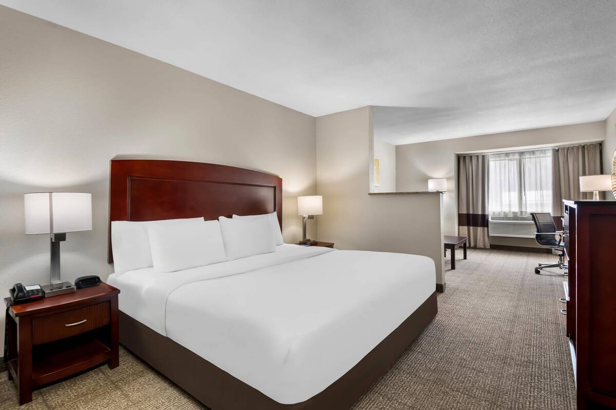 A hotel room with a large bed, bedside tables with lamps, a desk with a chair, and a window with curtains.
