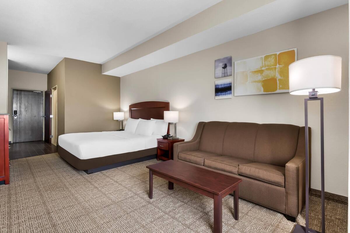 A hotel room with a bed, a sofa, a coffee table, a lamp, and artwork on the wall.