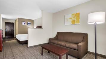 Una habitación de hotel con un sofá marrón, una mesa de centro de madera, una lámpara y una cama.