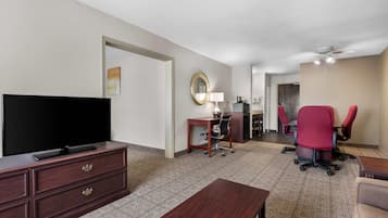 Habitación de hotel con televisión de pantalla plana, cómoda de madera, escritorio con silla y una silla de oficina roja, además de un ventilador de techo.