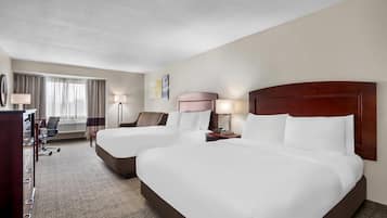 A hotel room with two beds, a desk, a chair, and a window with curtains.