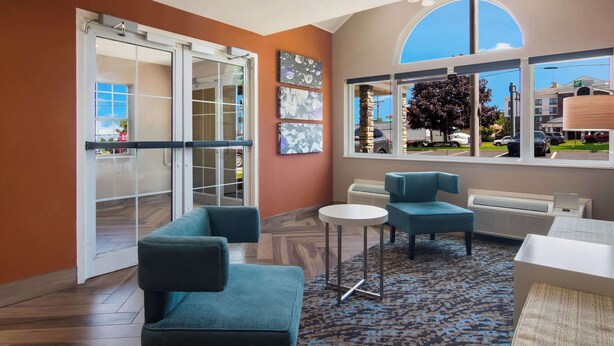 A modern lounge area with a glass door leading to a balcony, a seating area with a round table, and artwork on the wall. - Sleep Inn Erie near Sports Center (Erie)