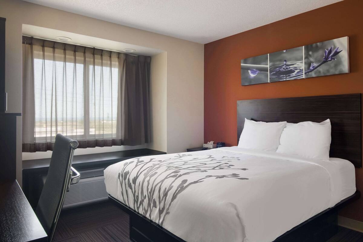 A hotel room with a large bed, a desk, a chair, and a window with curtains.
