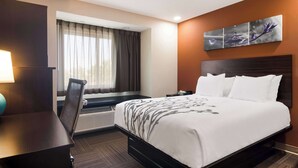 A hotel room with a large bed, a desk, a chair, a window with curtains, a wall-mounted artwork, and a nightstand. - Sleep Inn Erie near Sports Center (Erie)