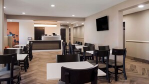 A modern restaurant with a central counter, multiple tables and chairs, and a flat-screen TV mounted on the wall. - Sleep Inn Erie near Sports Center (Erie)