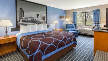 Habitación de hotel con una cama grande, dos mesitas de noche con lámparas, un escritorio con computadora, una silla y una ventana con cortinas.