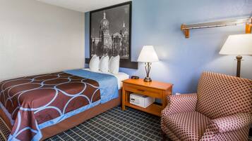 Habitación de hotel con cama, mesita de noche, lámpara, silla y perchero en la pared.