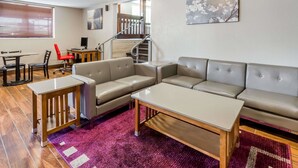A modern living room with a sofa, a coffee table, and a dining area with a table and chairs. - Super 8 by Wyndham Iowa City/Coralville (Coralville)