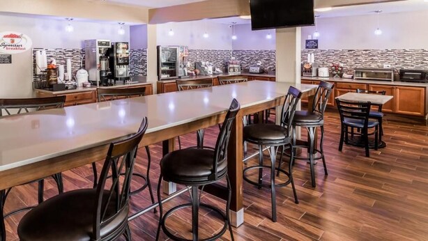 A spacious breakfast area with a long counter, multiple chairs, and a kitchen in the background. - Super 8 by Wyndham Iowa City/Coralville (Coralville)