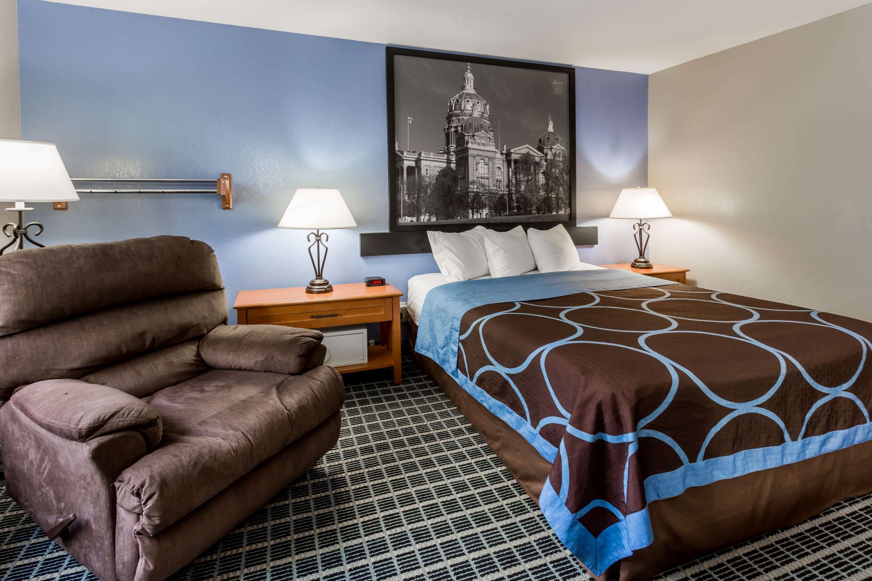 A hotel room with a king-sized bed, a brown leather sofa, two bedside tables with lamps, and a large black and white cityscape painting on the wall.