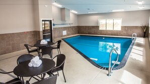 Un espace piscine doté d’un sol carrelé, d’une piscine à l’intérieur bleu et d’un coin salon avec des chaises et une table.