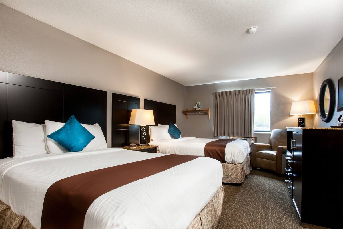 A hotel room with two beds, a desk, a chair, a coffee machine, and a TV.