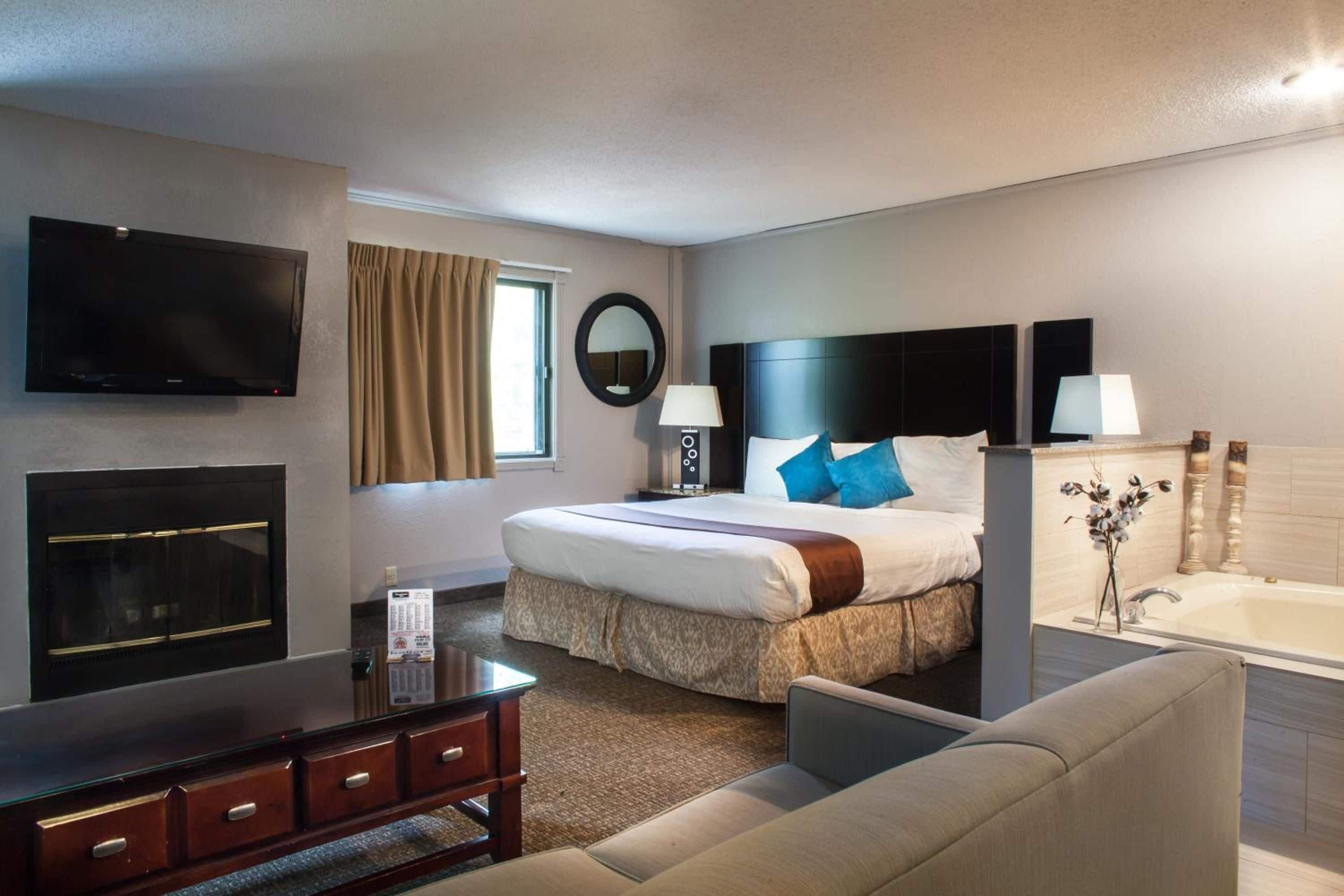 Een hotelkamer met een bed, een televisie, een bureau, een stoel, een raam met gordijnen, een spiegel, een lamp en een bad.