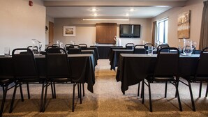 Une salle de conférence équipée de plusieurs tables et chaises, d’un téléviseur et d’un buffet en bois.