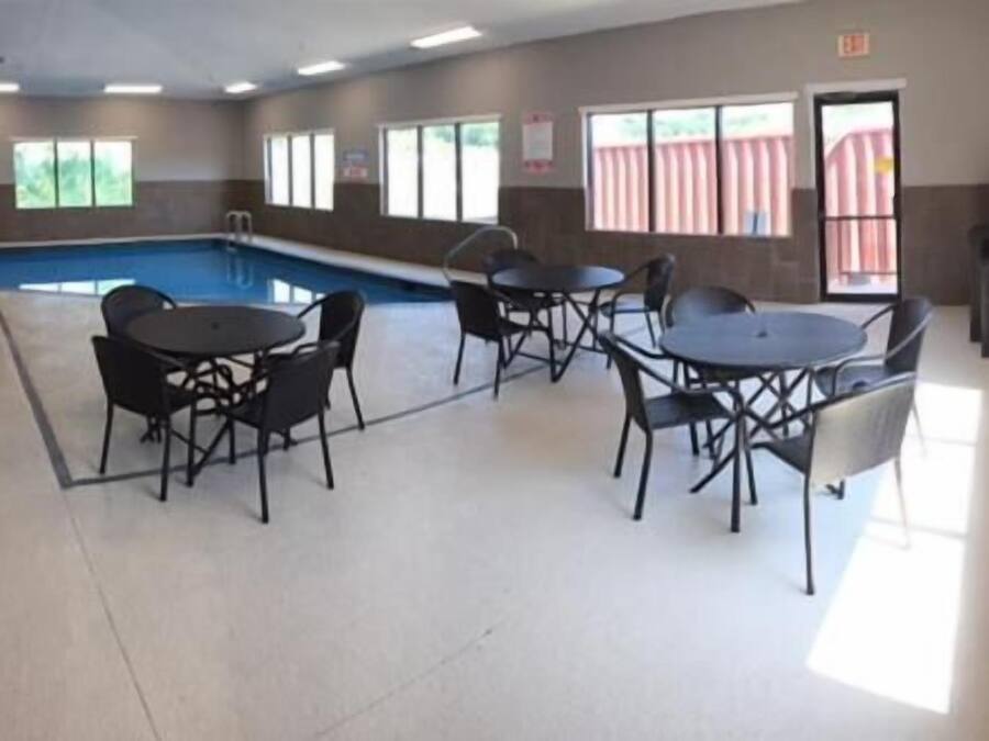 A swimming pool area with four tables and chairs, large windows, and a view of a red fence outside.