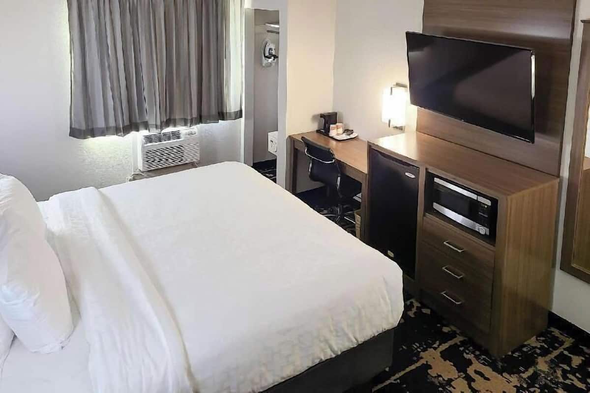 A hotel room with a bed, a desk with a chair, a television, and a wardrobe.