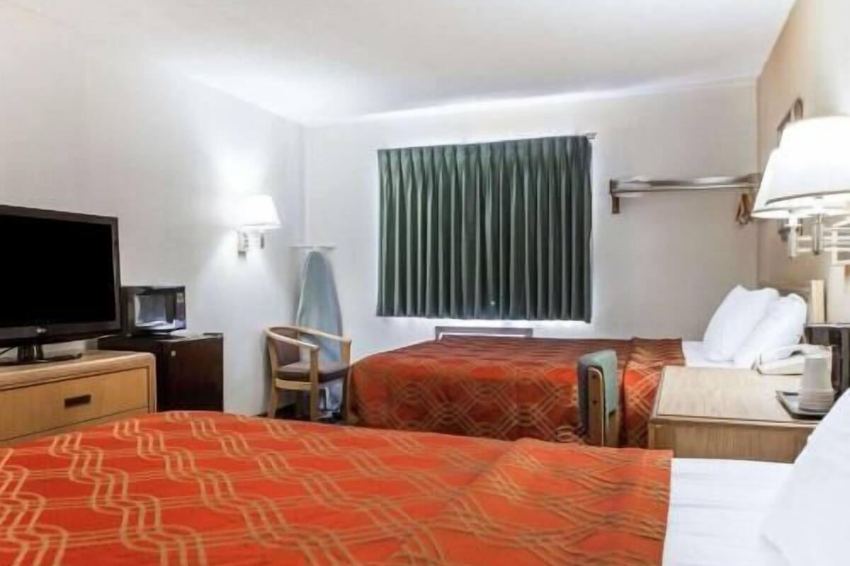 A hotel room with two beds, a television, a desk with a lamp, and a window with curtains.