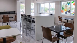 A modern indoor dining area with multiple tables and chairs, a central island, and large windows with heart-shaped decorations. - Clarion Pointe Bettendorf - Quad Cities (Bettendorf)