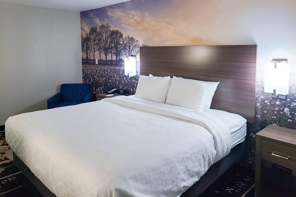 Habitación de hotel con una cama grande, una silla azul, una mesita de noche con una lámpara y un mural en la pared.