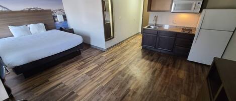 Habitación de hotel pequeña con cama, kitchenette y piso de madera.