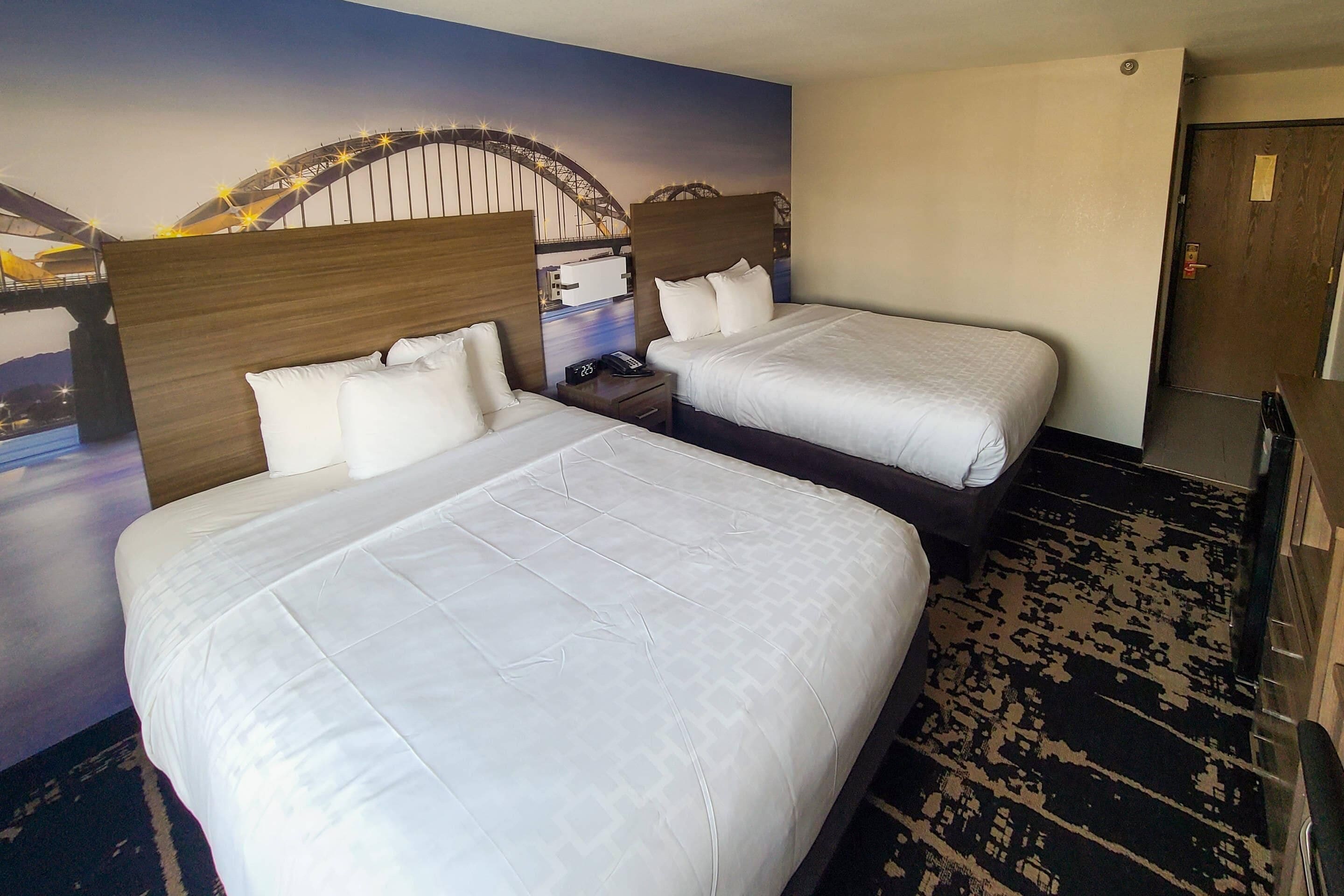 A hotel room with two beds, a mural of a bridge, and a patterned carpet.