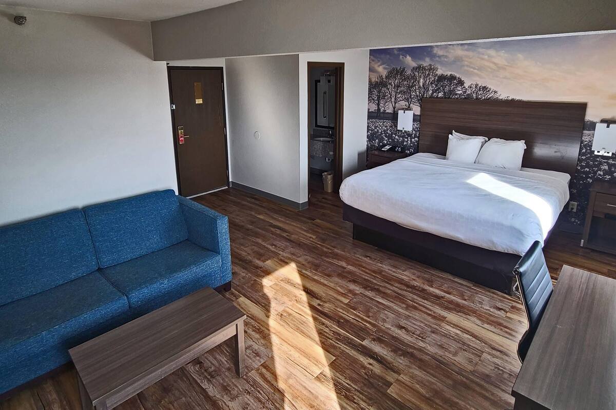 A hotel room with a bed, a blue sofa, a wooden coffee table, and a desk.